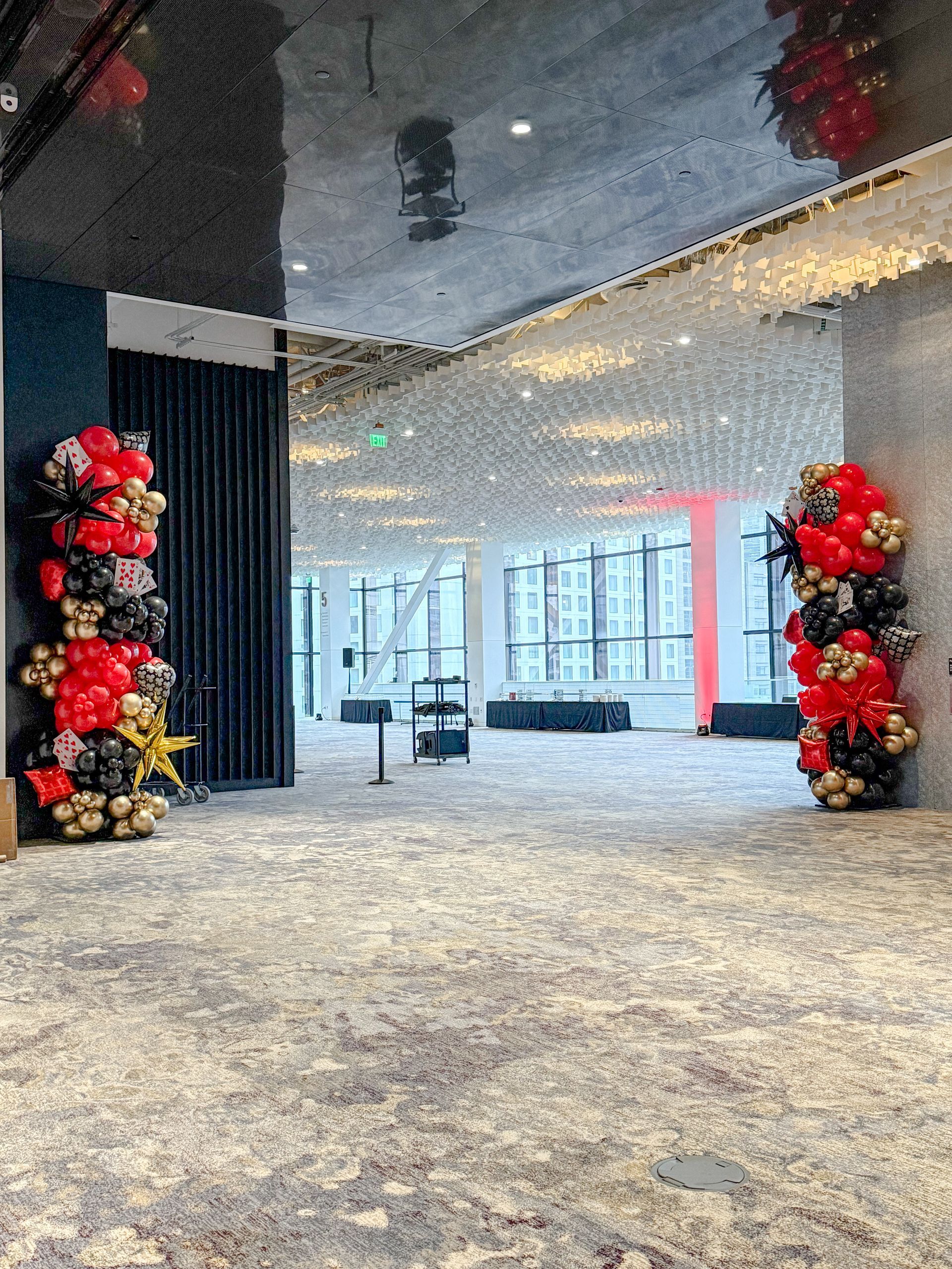Entrance to a decorated event space with balloon columns. Black, red, and gold balloons flank the doorway.