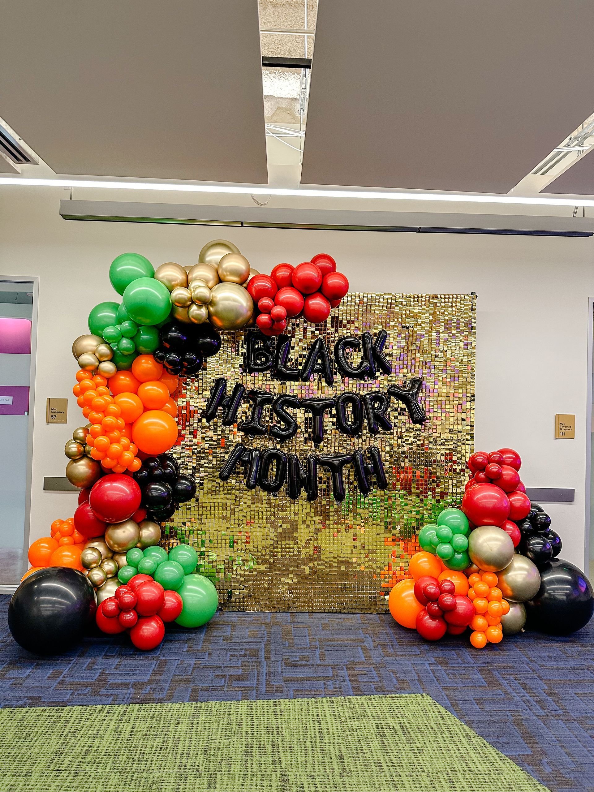 colorful balloon garland against a gold shimmer wall with the words black history month on it