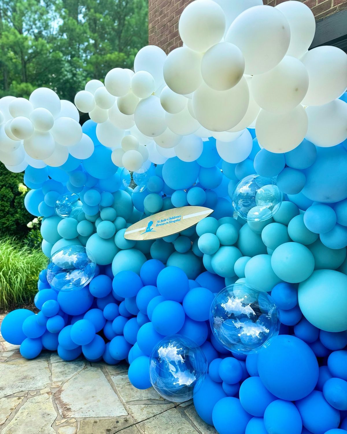 A balloon arch featuring a gradient from white at the top to shades of blue, with clear bubble balloons interspersed.