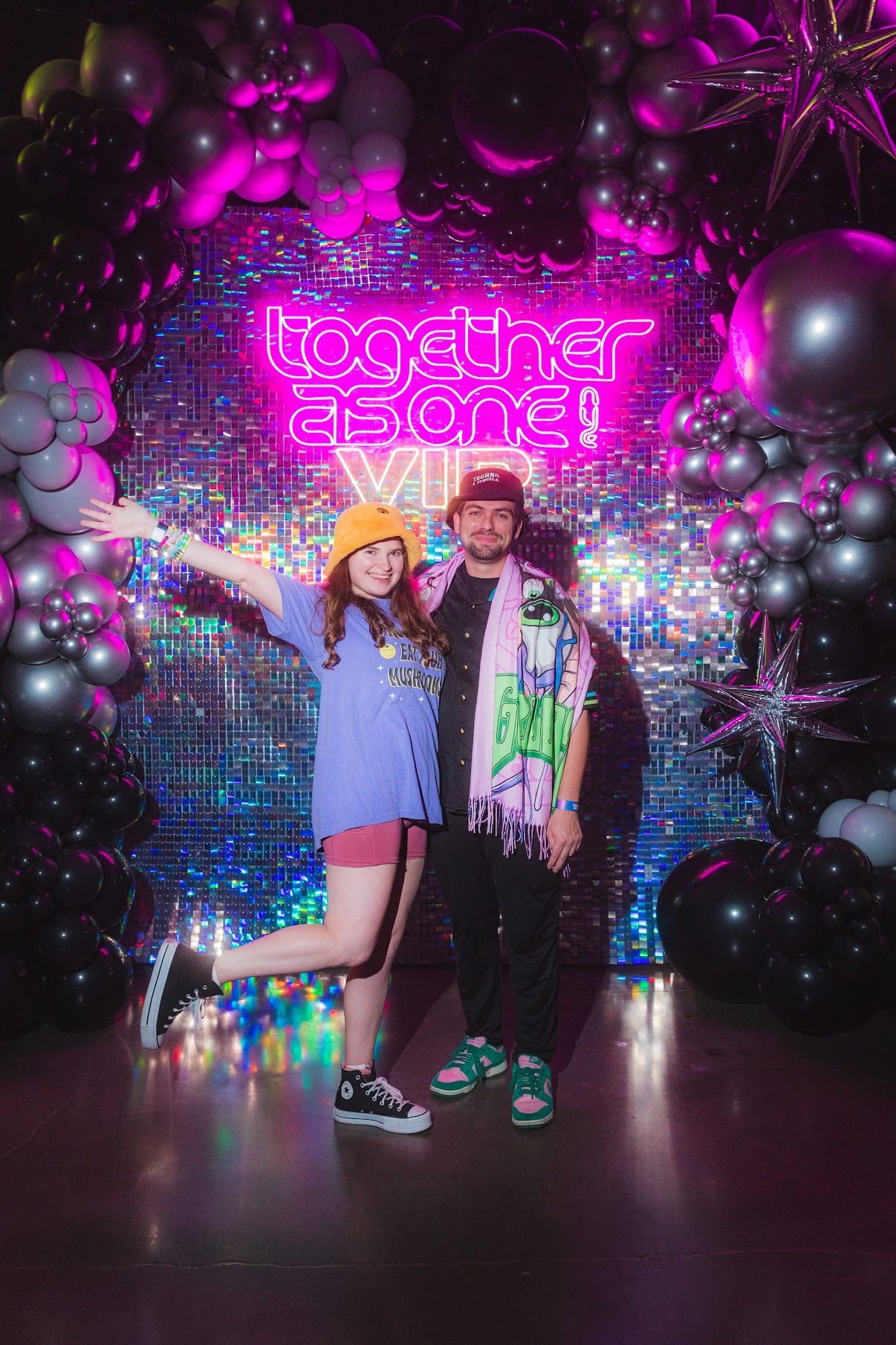 Two people pose in front of a neon