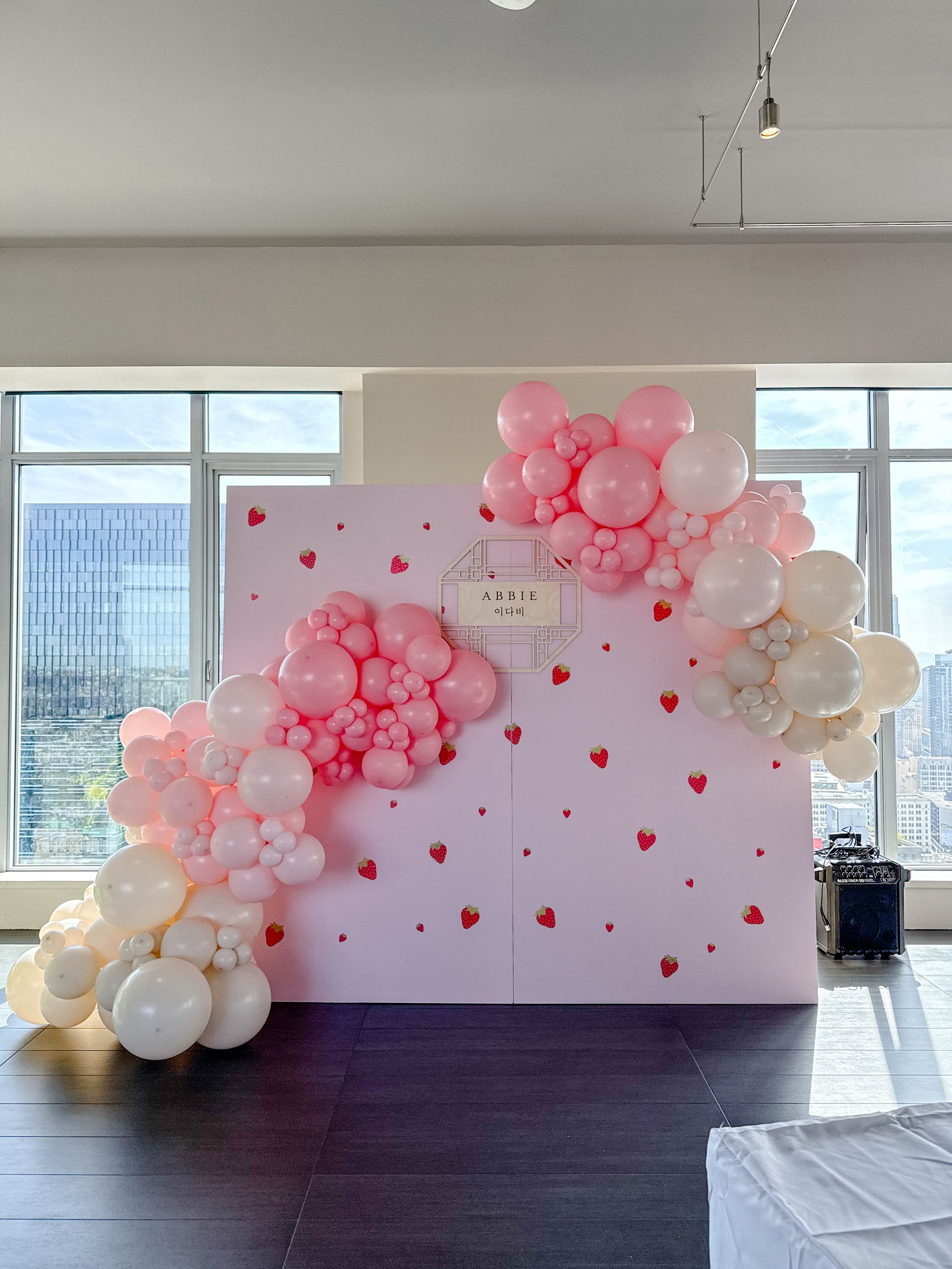 A pink backdrop decorated with strawberry decals and a cascading balloon arch in shades of pink, white, and cream.
