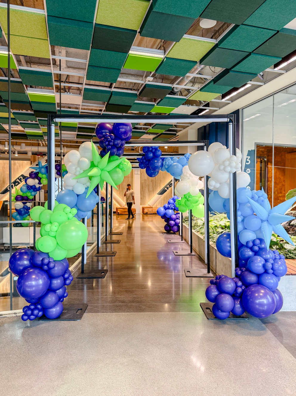 Archway decorated with blue, green, and white balloons, leading into a building hallway.