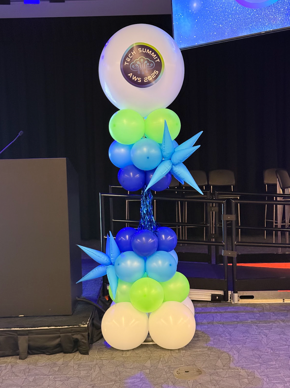 Balloon sculpture: a pillar with white, blue, and green balloons, topped with a large white balloon displaying a logo.
