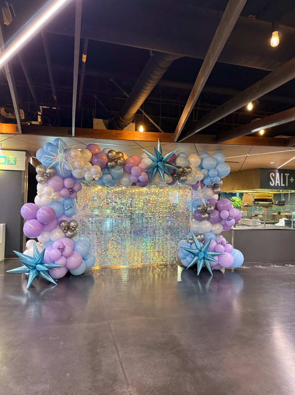 Rainbow balloon archway at a glass door entrance, on a stone patio.