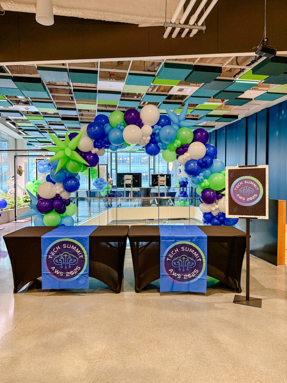 Balloon arch and branded signs framing a table in a colorful indoor event setup for the AWS Tech Summit