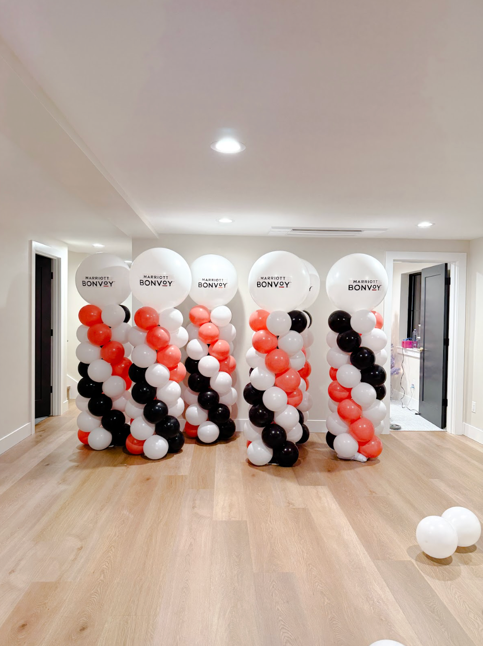 Five balloon columns in an indoor room, each topped with a large white balloon, featuring spirals of orange, black, white.