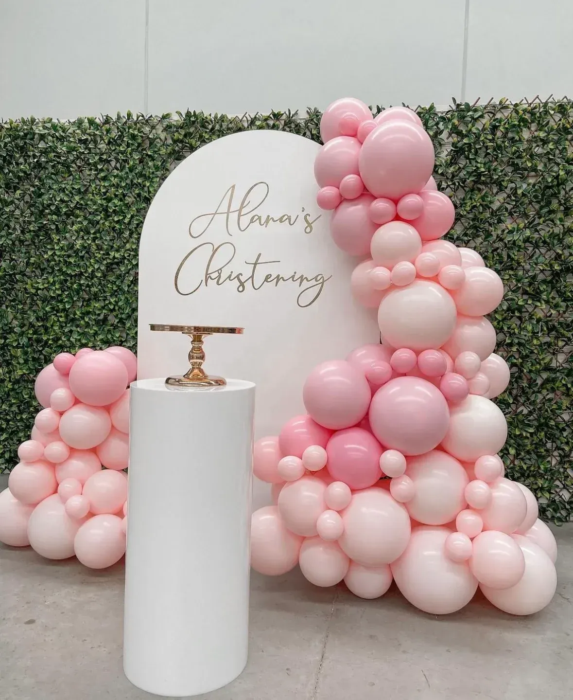 A white pillar surrounded by pink balloons for a baby girl 's christening.