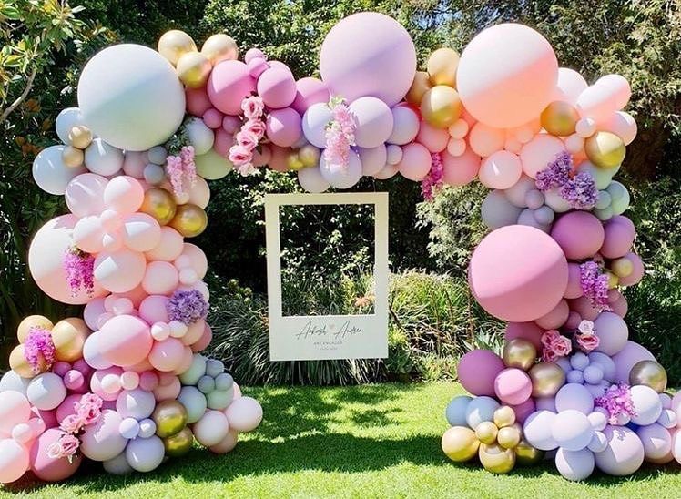 A picture frame is surrounded by balloons and flowers.