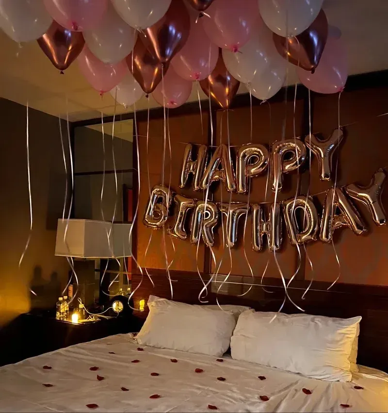 A bed with balloons hanging from the ceiling that say happy birthday