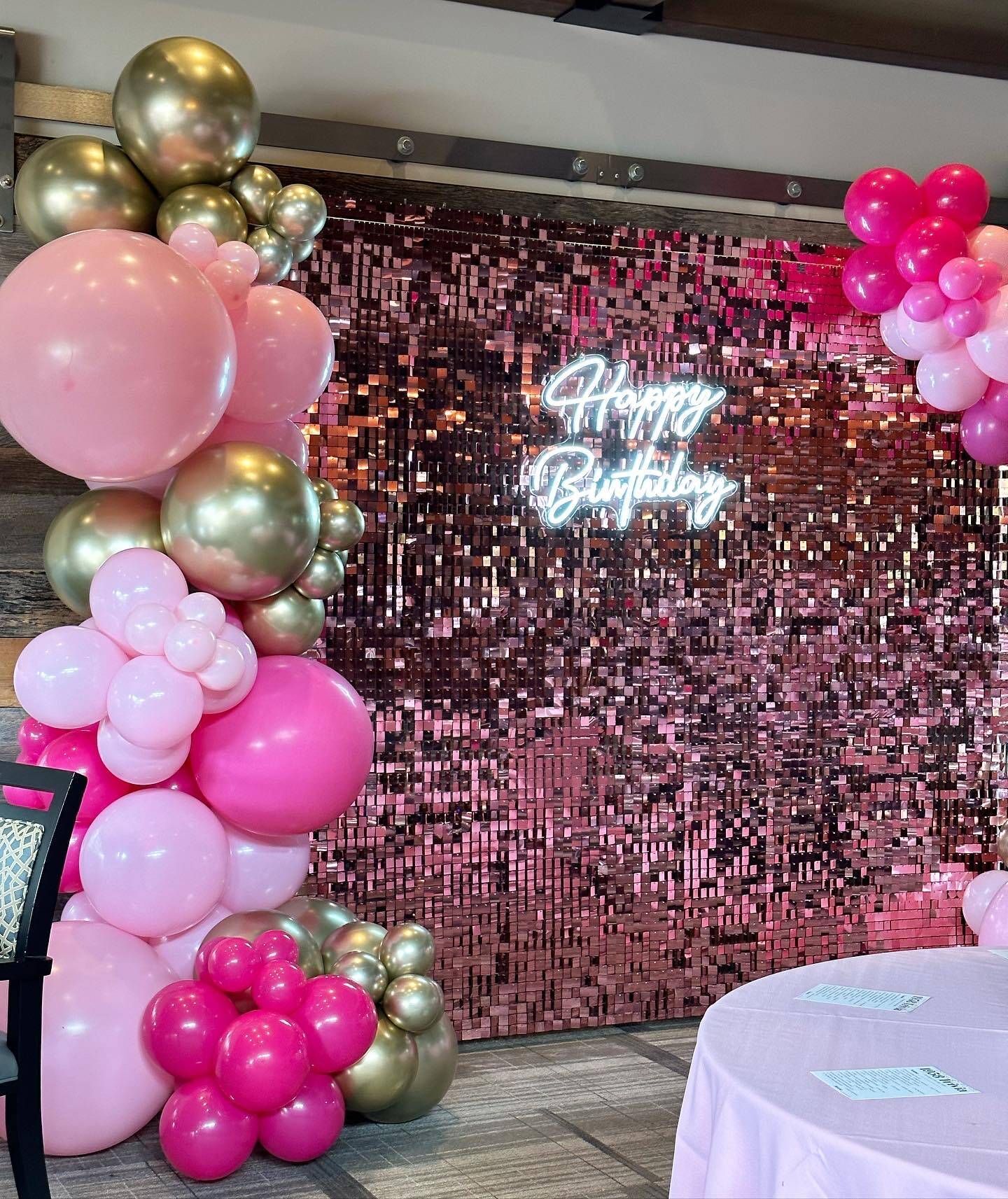 A room filled with pink and gold balloons and a neon sign that says `` happy birthday ''.