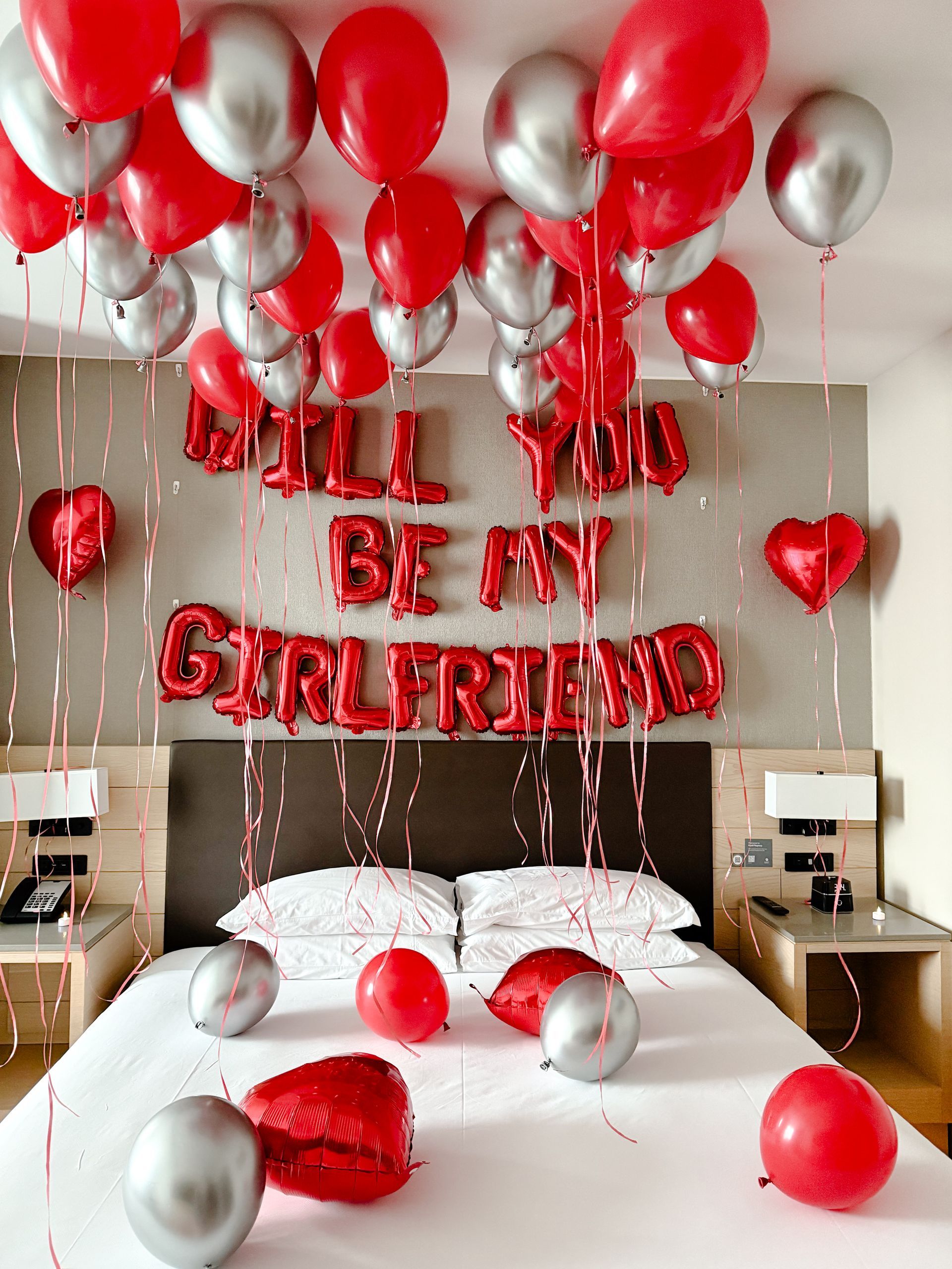 Bedroom decorated with red and silver balloons and “Will you be my girlfriend?” balloon letters above the bed