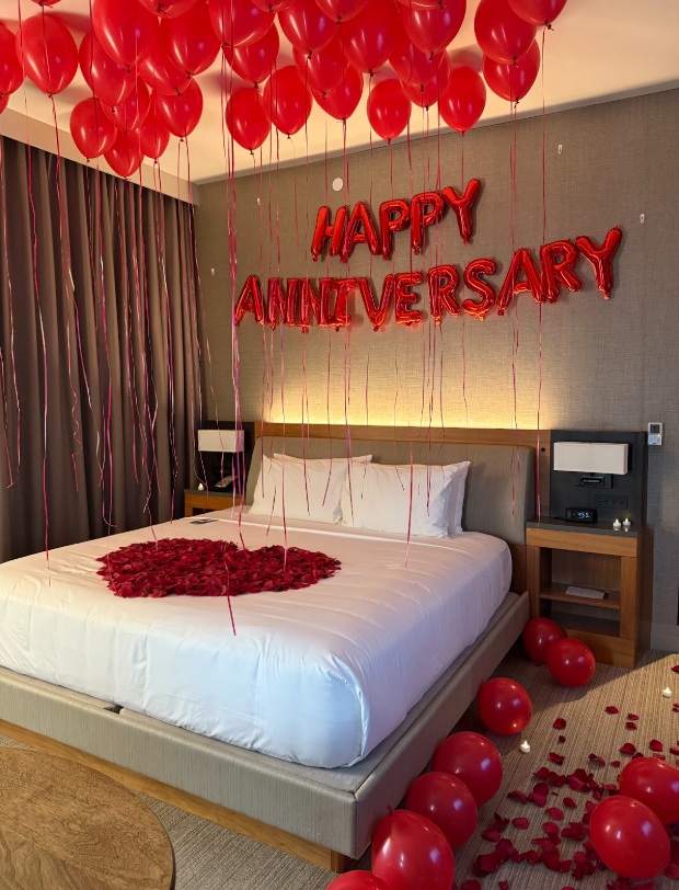 Romantic hotel room with red balloons and rose petals, bed decorated for a happy anniversary