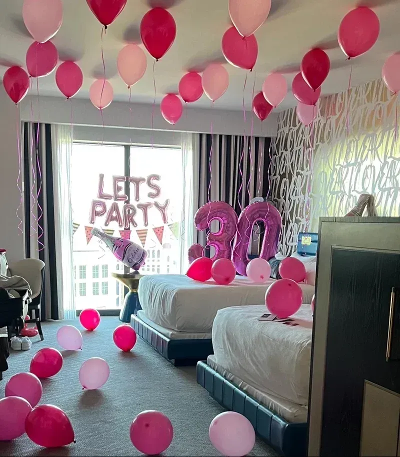 A hotel room decorated with pink balloons and a sign that says lets party