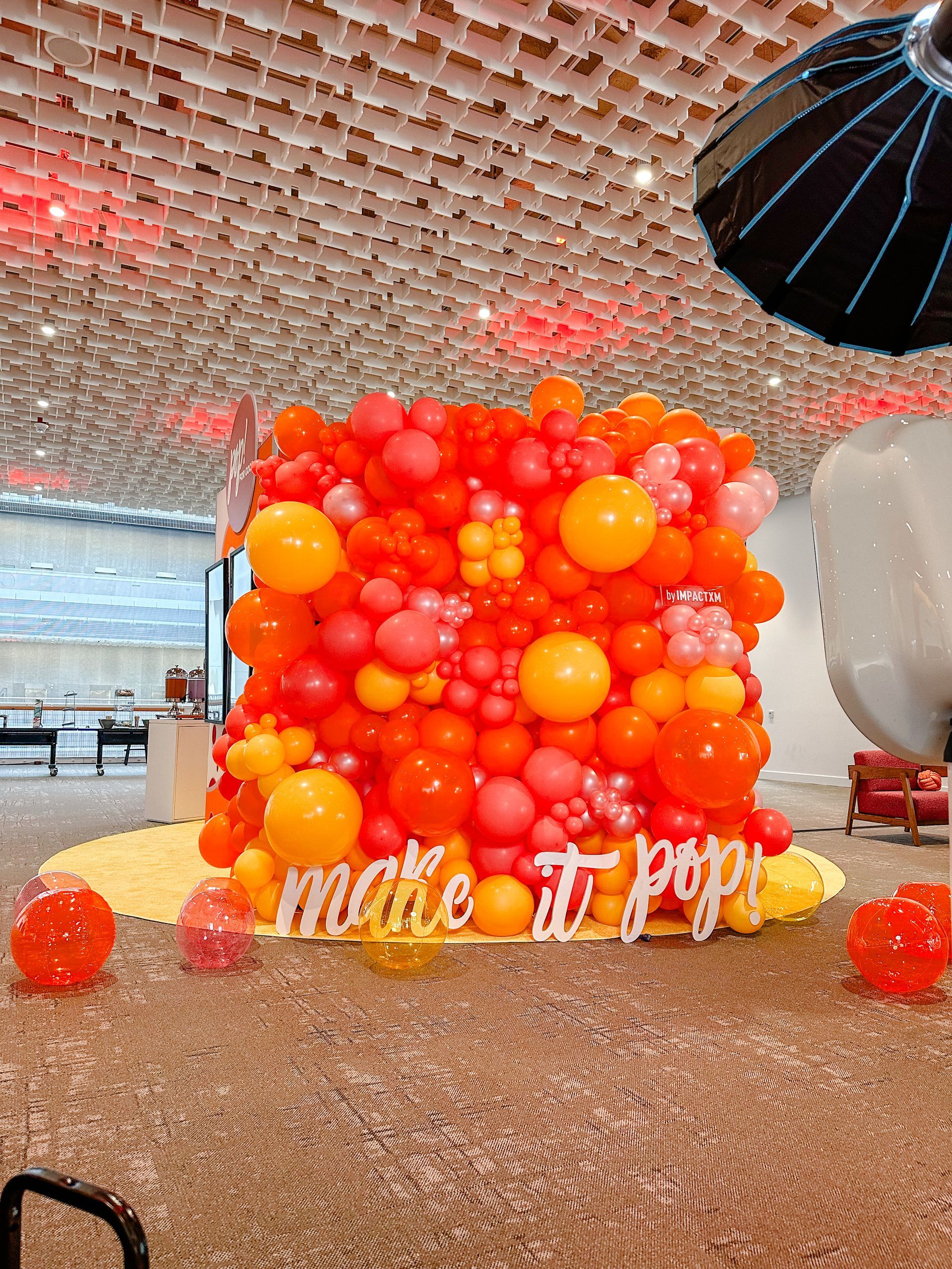 A wall of orange and pink balloons with a sign that says `` make it pop ''.