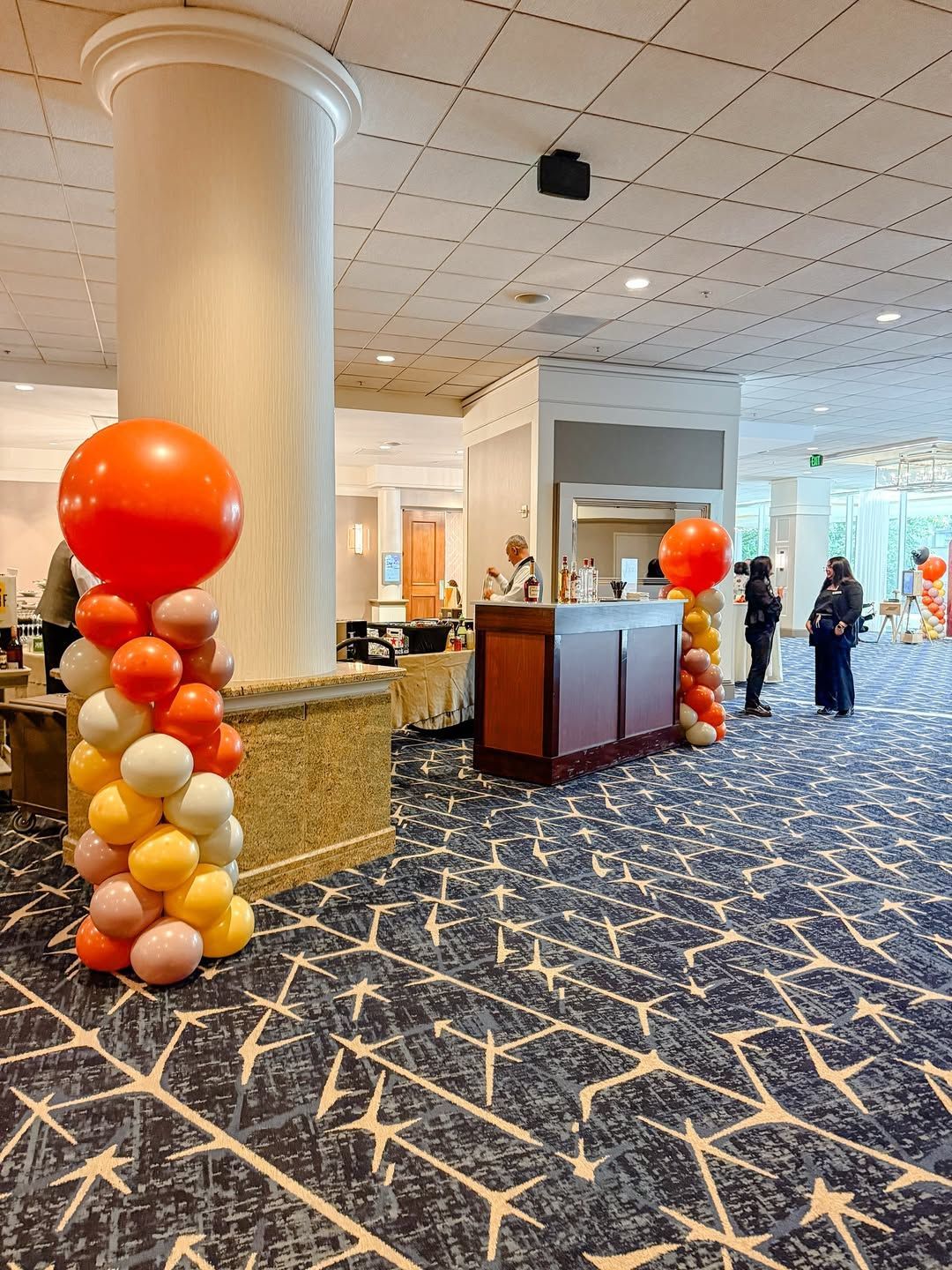 Hotel lobby with balloon towers, reception desk, and a few people standing near the entrance.