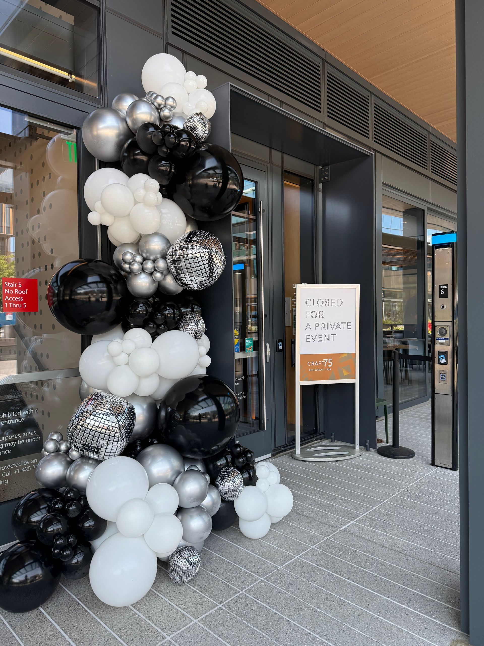 Black and white balloon arch framing a storefront entrance with a sign on the sidewalk