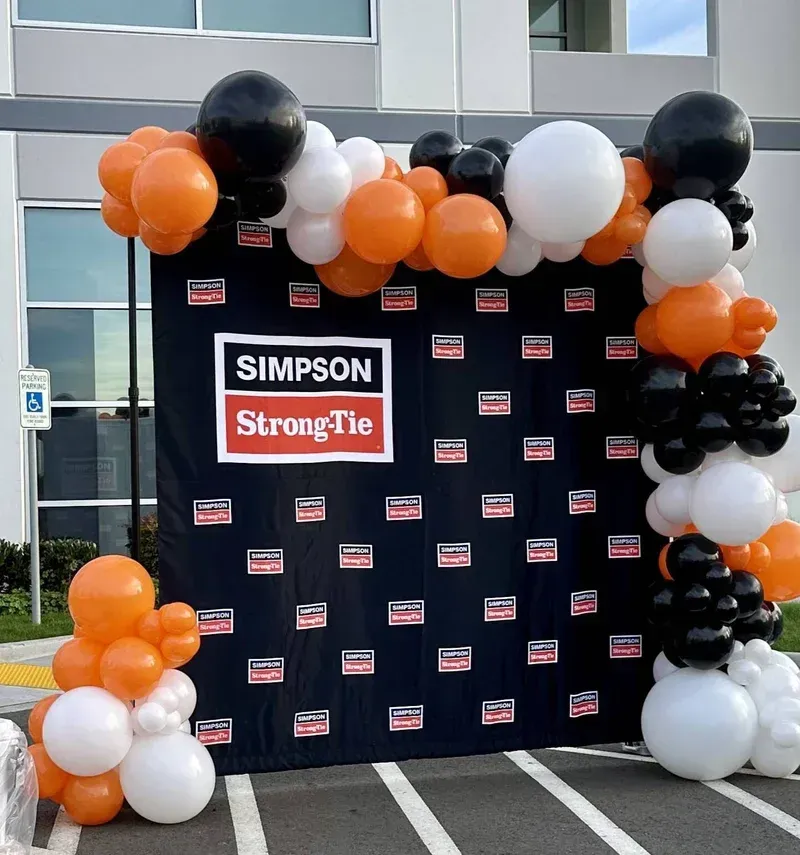 A simpson strong tie sign is surrounded by balloons in front of a building.