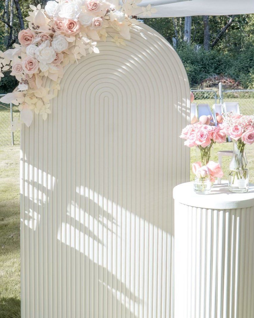 A white arch with pink flowers on it and a table with pink flowers on it.