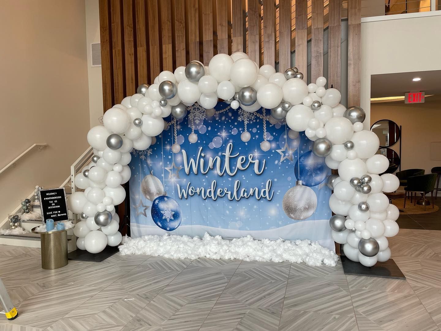 A large arch made of white and silver balloons in a room.