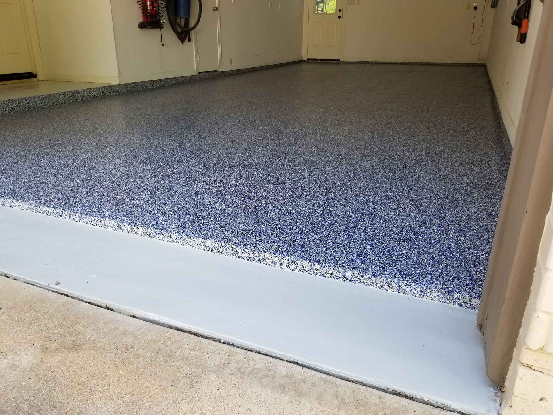 Check out this photo to view a pristine, multi-car garage floor transformation featuring a durable blue, black, and grey decorative flake coating seamlessly installed by Global Garage Flooring & Design.