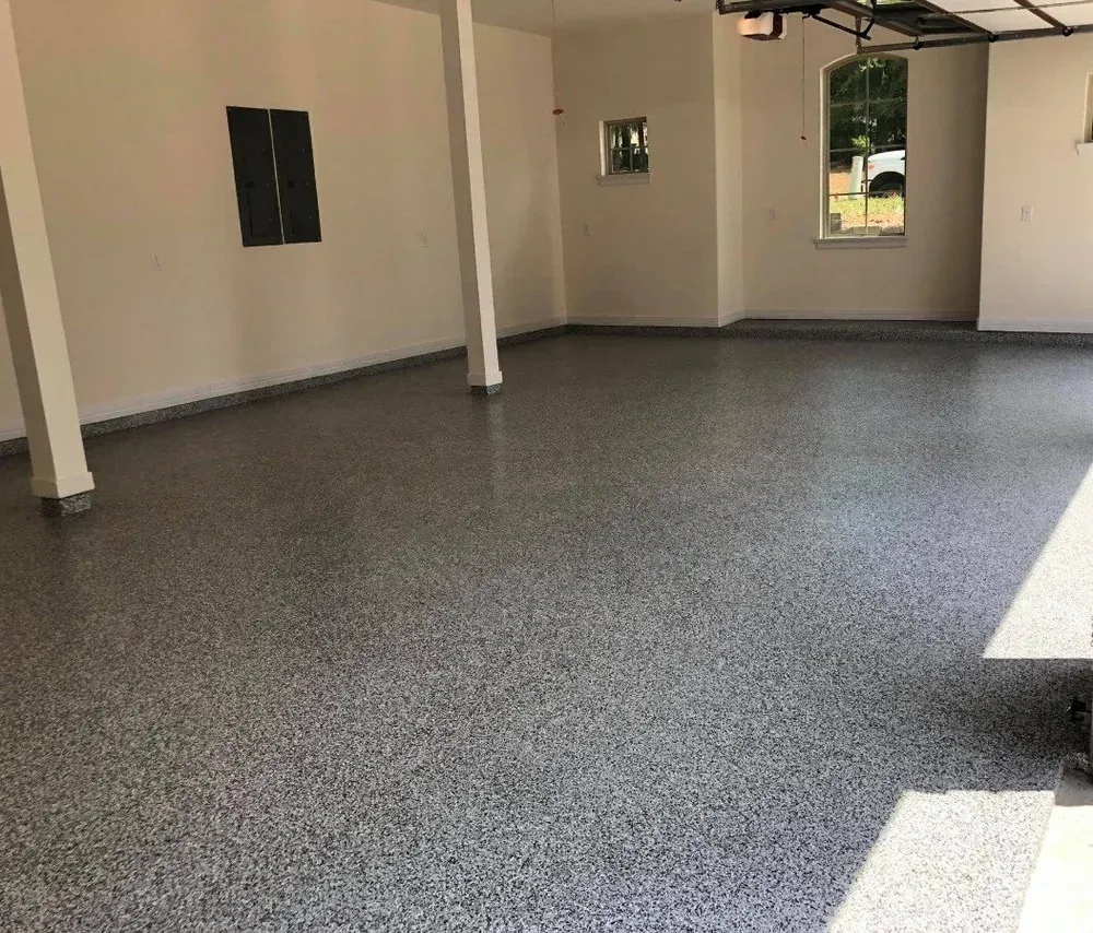 Empty covered patio with speckled gray flooring and beige walls, open to a grassy yard.