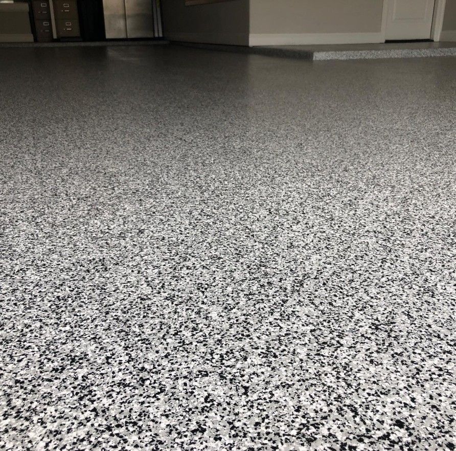 Look at this photo to see a newly finished, high-quality grey, black, and white epoxy flake coating system applied across a spacious residential garage floor by Global Garage Flooring & Design.