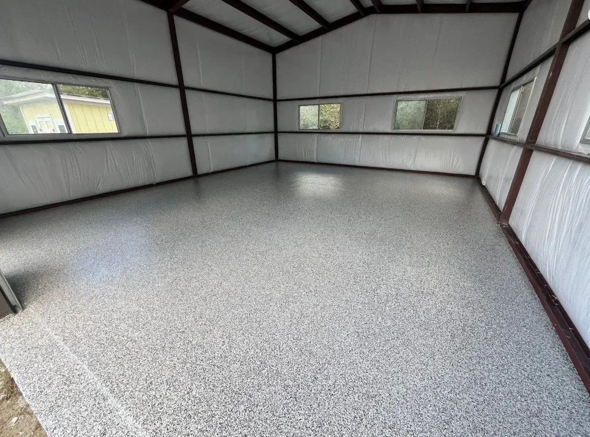 Empty metal storage shed with gray floor, white walls, and small windows.