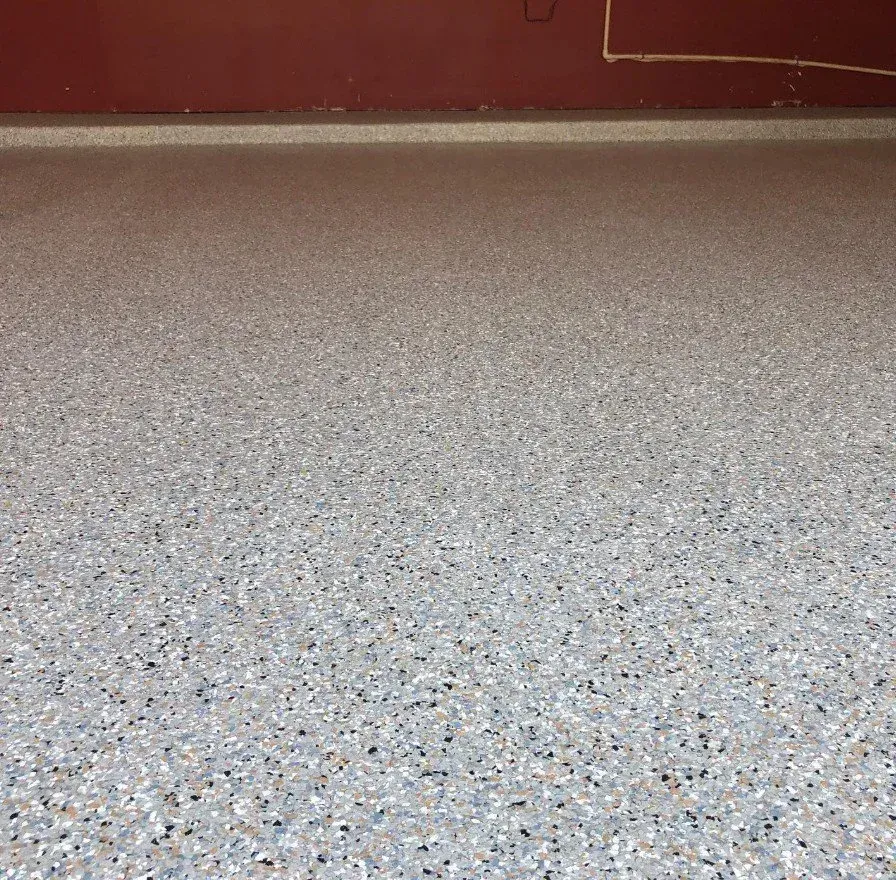 Empty speckled floor beside a maroon wall and baseboard strip