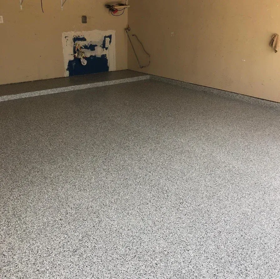 Empty beige room with a gray speckled floor and a small wall opening near the back.
