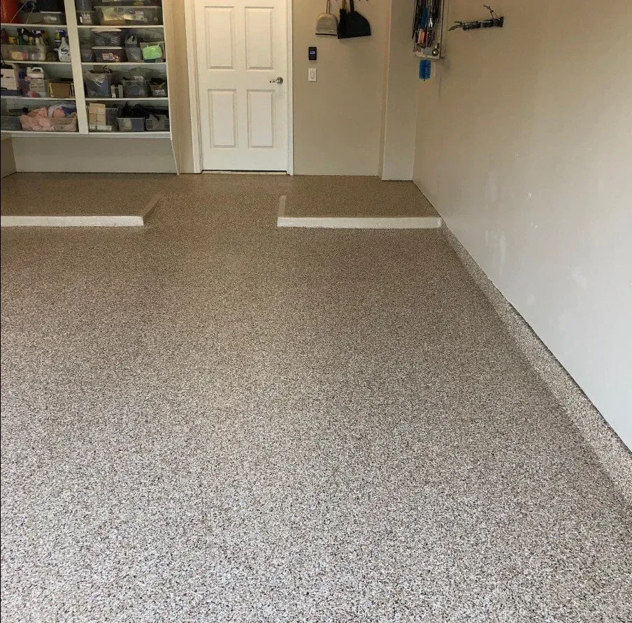 Empty garage with speckled epoxy floor, white walls, and storage shelves at the back