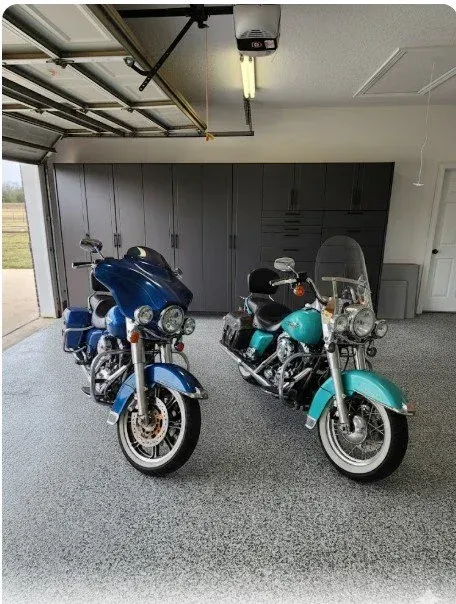 Two motorcycles, one blue and one teal, parked in a garage with the door open.