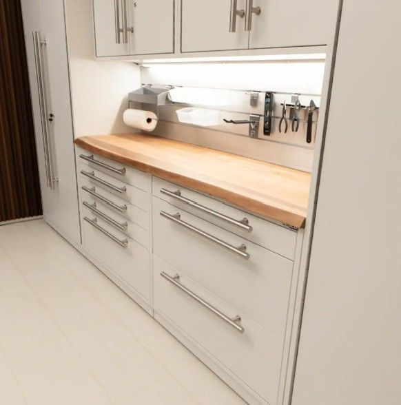 Clean white ProSlat LUX garage cabinetry with a warm live edge wood countertop and modern metal backsplash, offering a bright and functional workspace.  Designed by Global Garage Flooring & Design of Houston