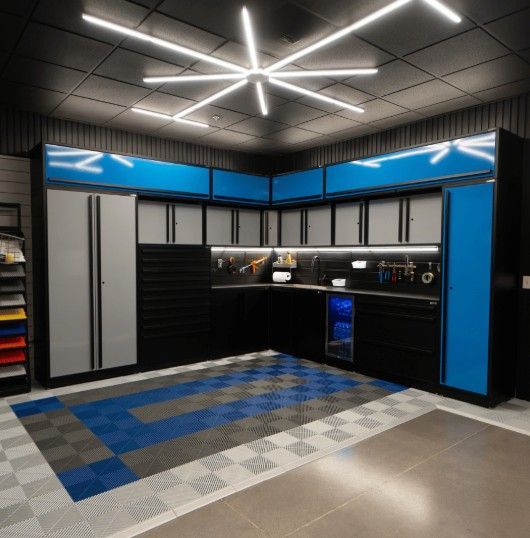 A premium L‑shaped ProSlat Fusion Plus garage workspace with blue upper cabinets, gray lower units, LED lighting, and a patterned SwissTrax floor for a high‑end finish.  ProSlat cabinets and SwissTrax flooring available at Global Garage Flooring & Design of Houston