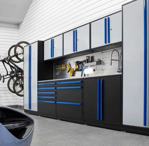 A clean, organized ProSlat FusionPlus garage featuring black and gray cabinets with blue accents, a stainless backsplash, and a built‑in utility sink.   Design and installation available at Global Garage Flooring & Design of Houston