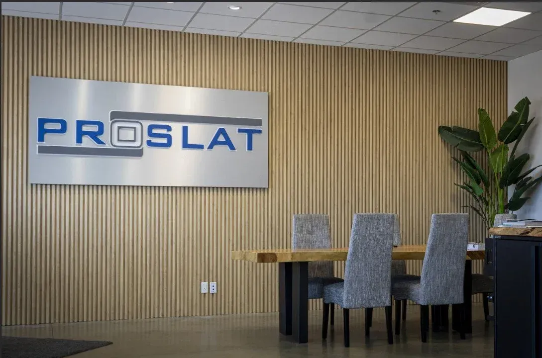 Office lobby with PROSLAT sign, wooden wall, table, chairs, and a potted plant