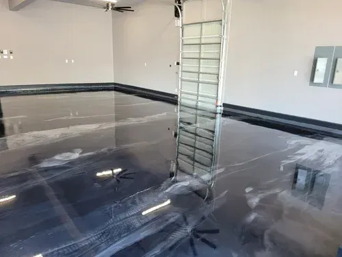 Shiny epoxy garage floor reflecting light, with a ladder and wall-mounted panel in a clean empty garage