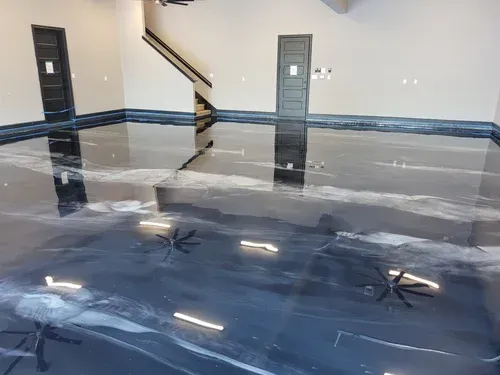 Empty room with a glossy gray epoxy floor reflecting lights and stairs, with two doors on the back wall