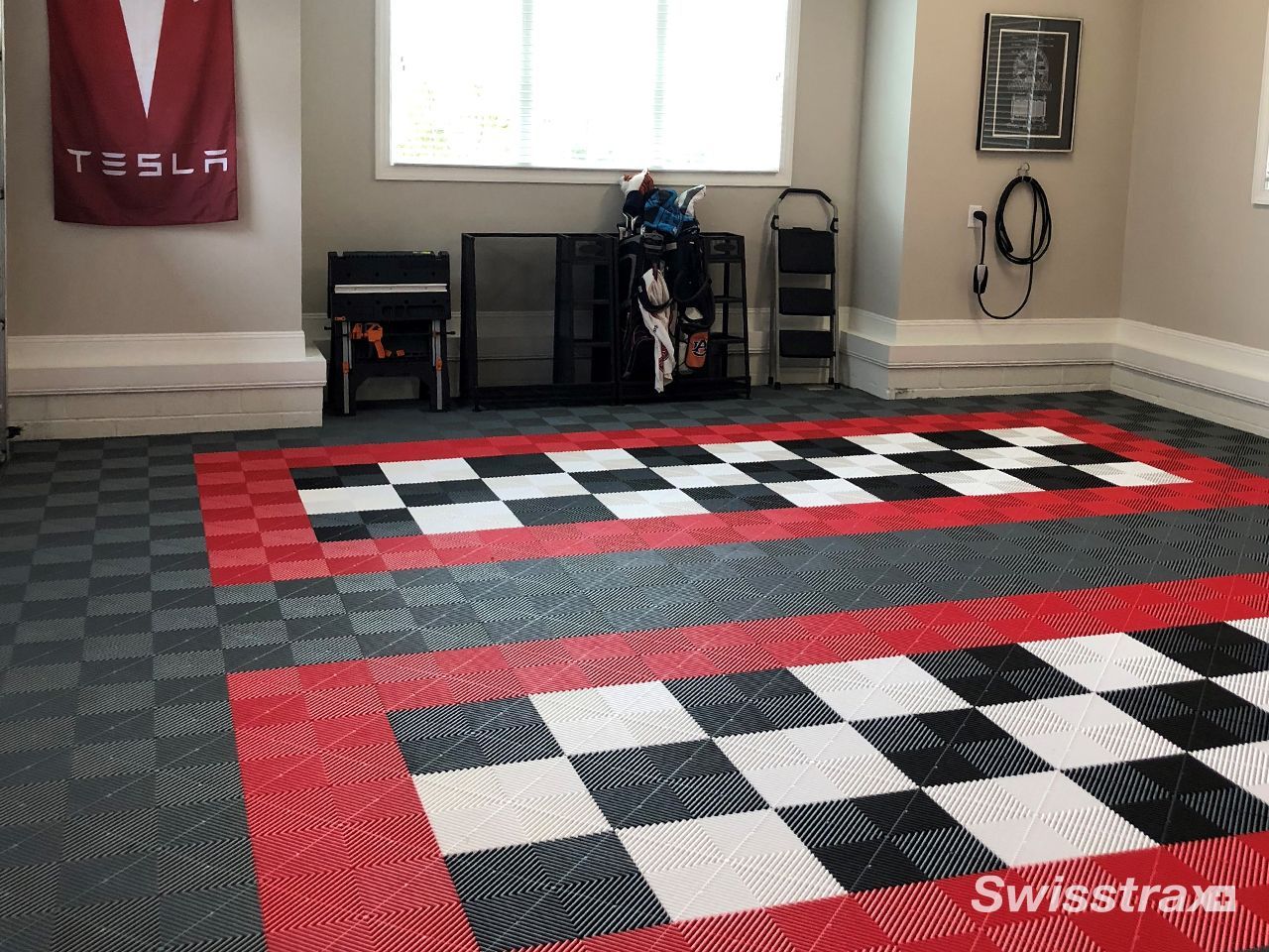 View a garage featuring a clean residential garage setup with a Tesla charging station and a custom red, white, grey, and black checkered SwissTrax interlocking tile floor.