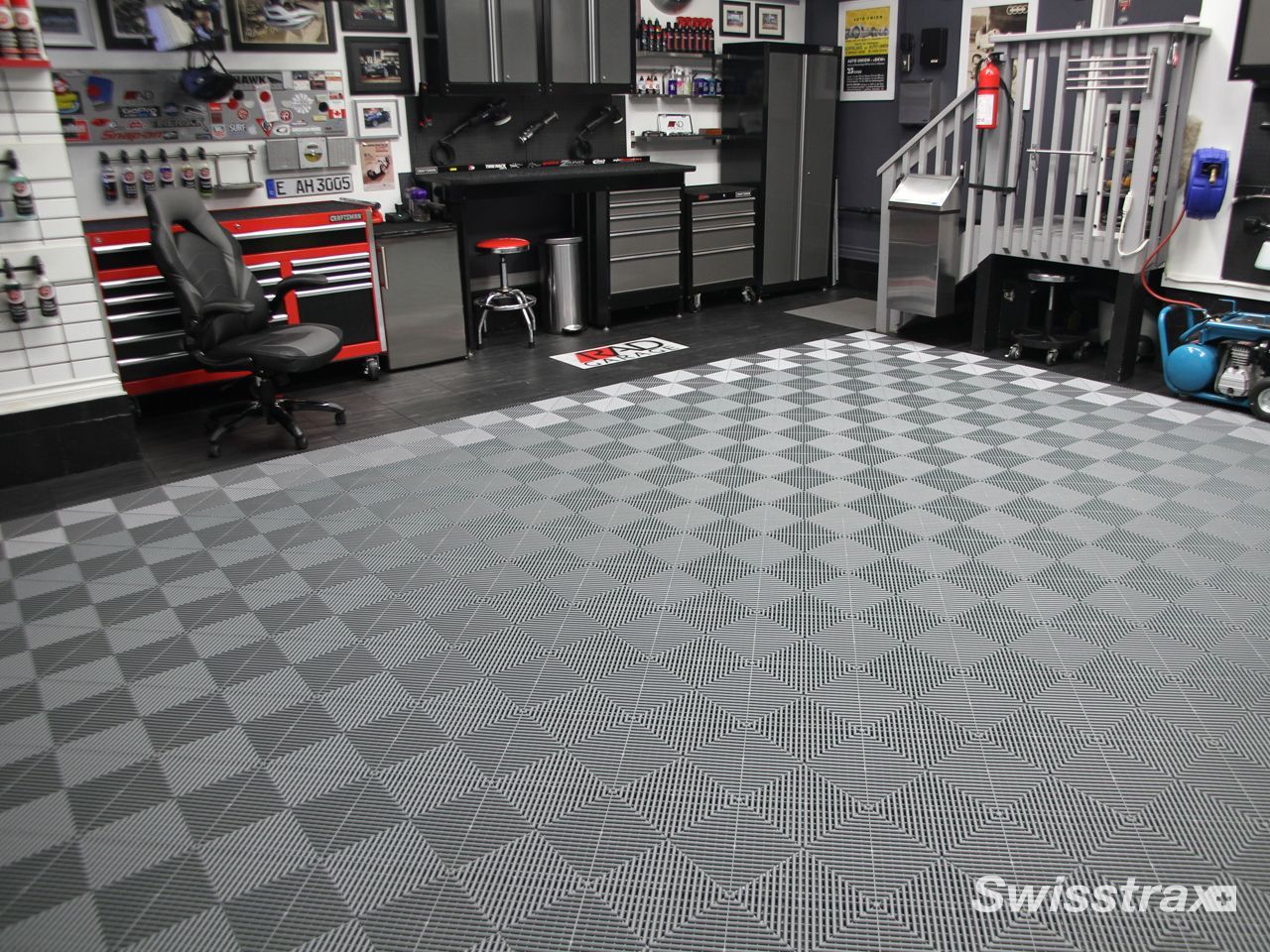 Explore a garage to see a premium custom garage setup with sleek grey cabinetry and a striking grey SwissTrax tile floor outlined with a white checkered border.