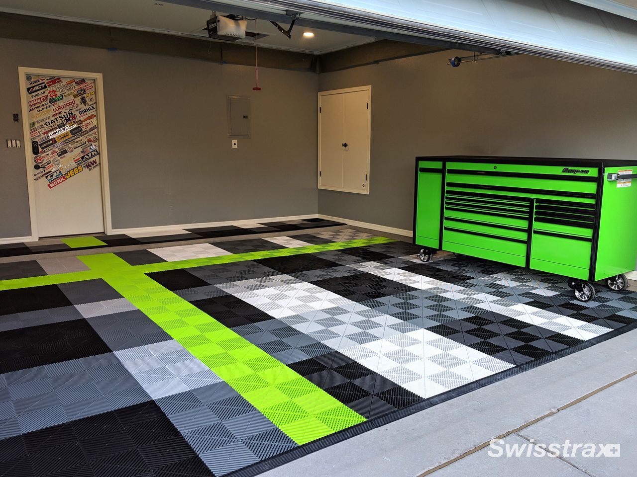 Check out a garage featuring black,  white and grey patterned SwissTrax interlocking tile floor with green accent tiles and matching green cabinets.