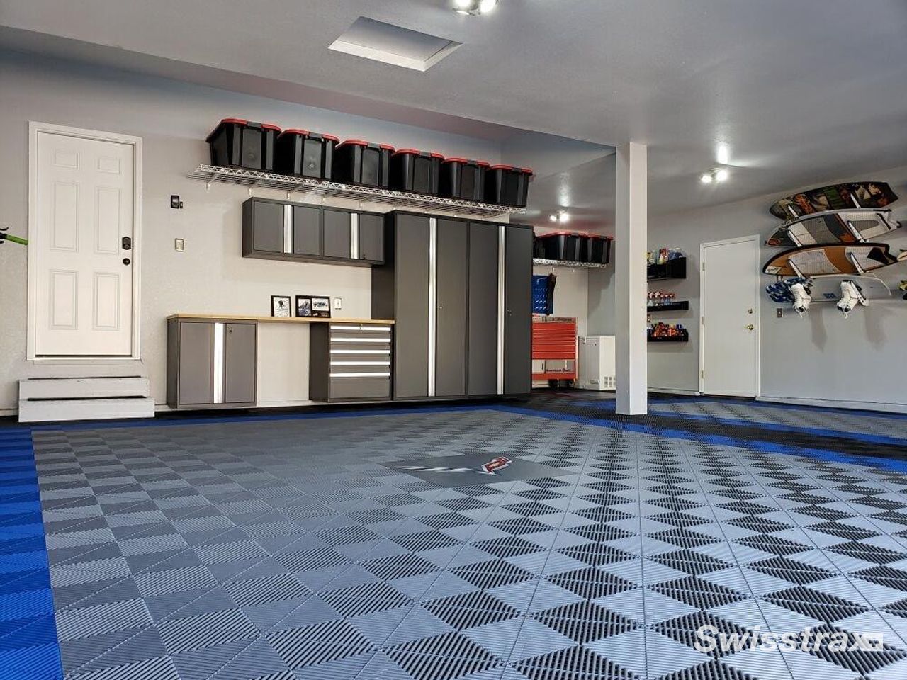 Explore a garage to see a premium custom garage setup with sleek black cabinetry and a striking grey SwissTrax tile floor outlined with a vibrant red border.