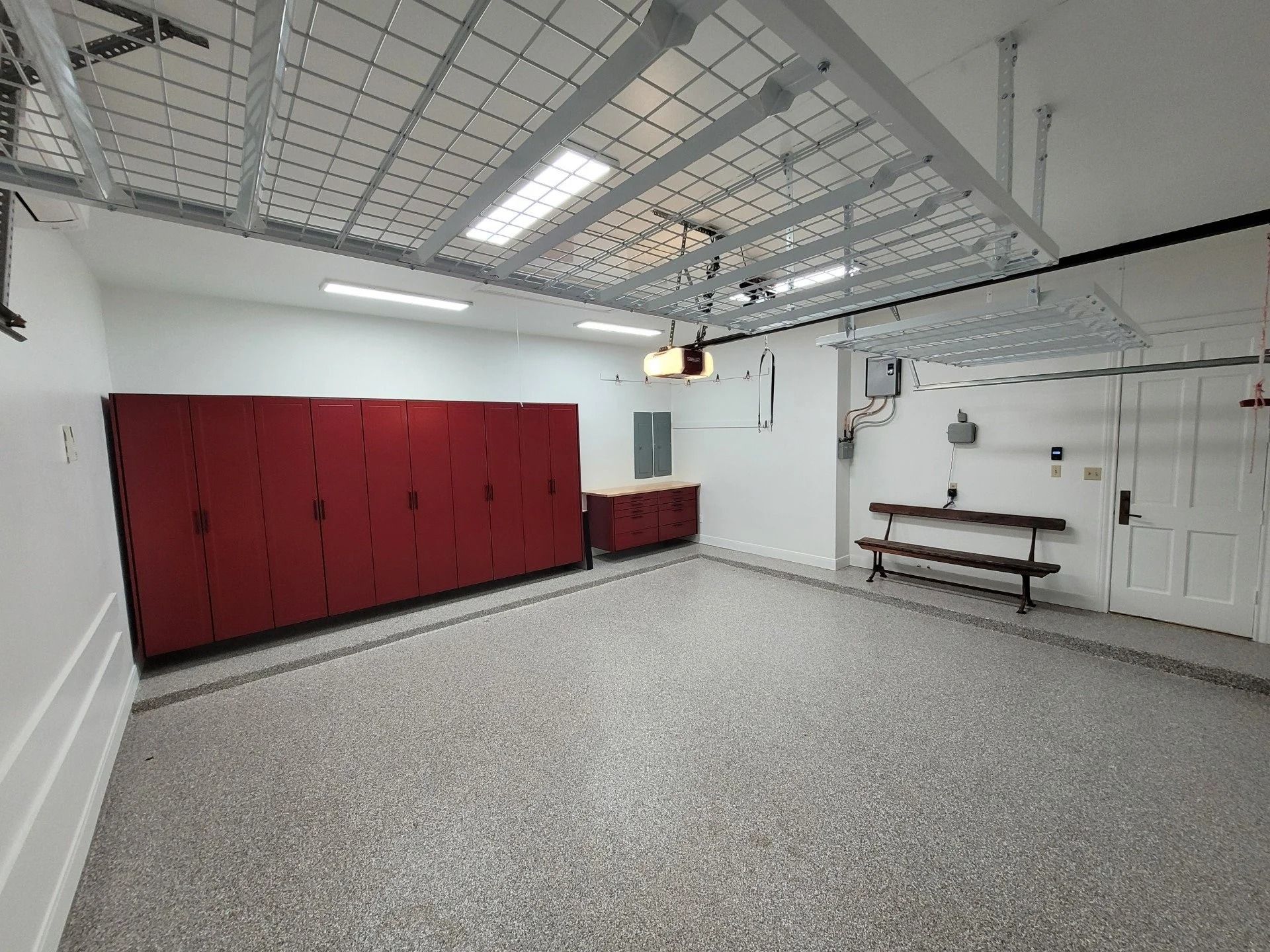 Empty garage interior with red lockers, white walls, and a workbench under ceiling lights