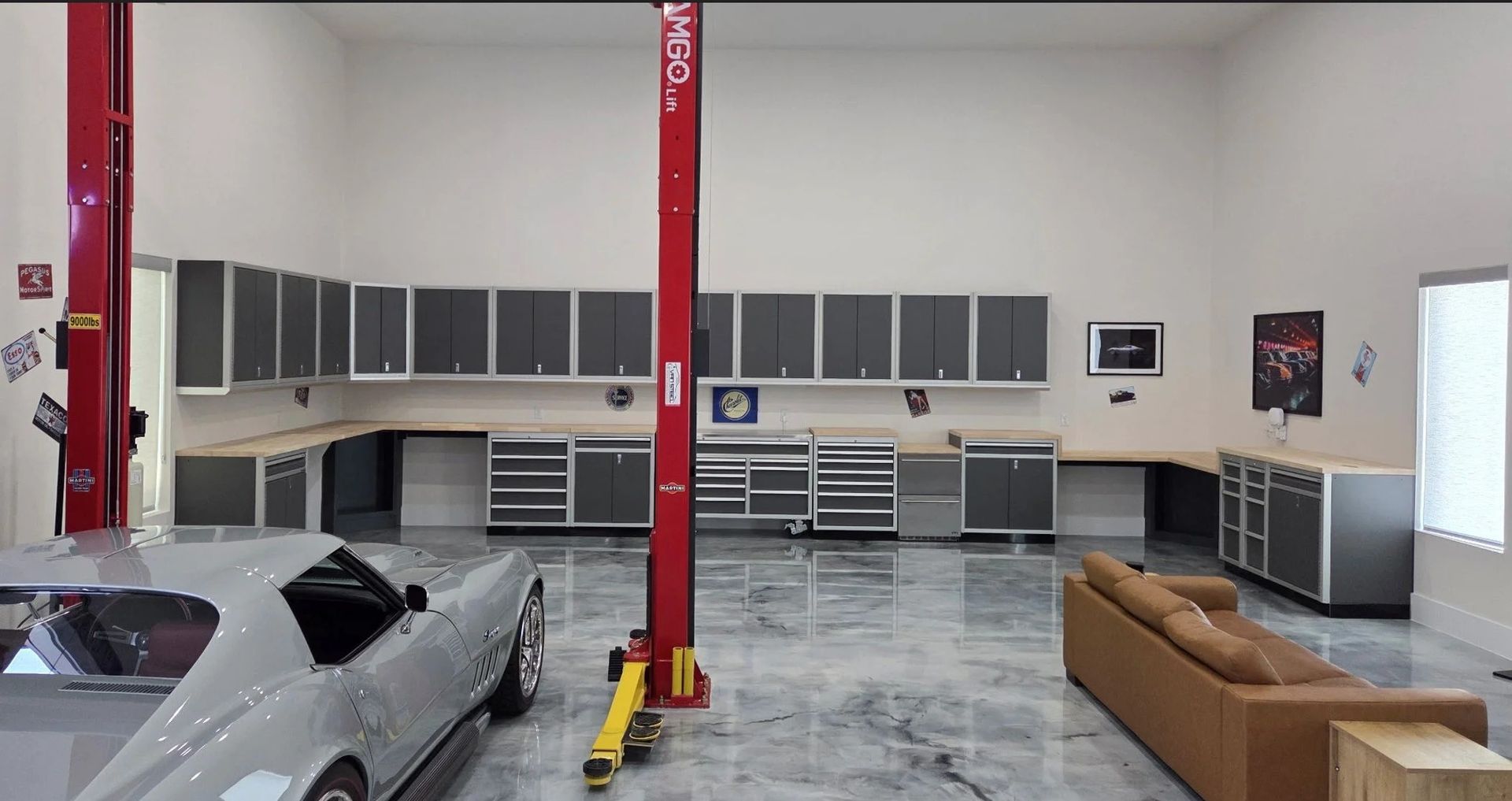 A wider look at a breathtaking ultimate vehicle sanctuary setup, showcasing an extensive wall-to-wall Moduline Aluminum Cabinet system alongside a classic Corvette, bright recessed lighting, and premium metallic floors.