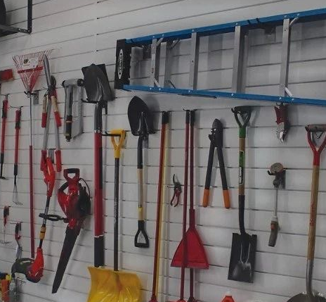 Garden tools hanging on a slatwall display, including shovels, rakes, and ladders.