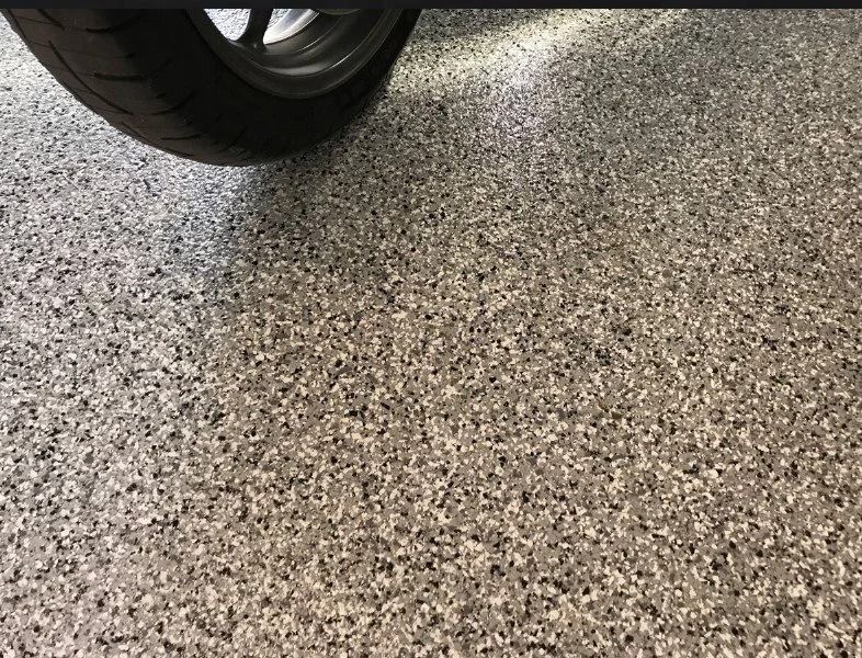 Get a close-up look at a durable garage floor application of a Polyaspartic Flake floor by Global Garage Flooring & Design Houston highlighting a textured blend of black, white, and gray decorative vinyl chips
