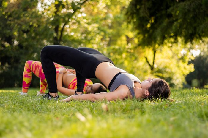 Two women are doing yoga in the grass in a park