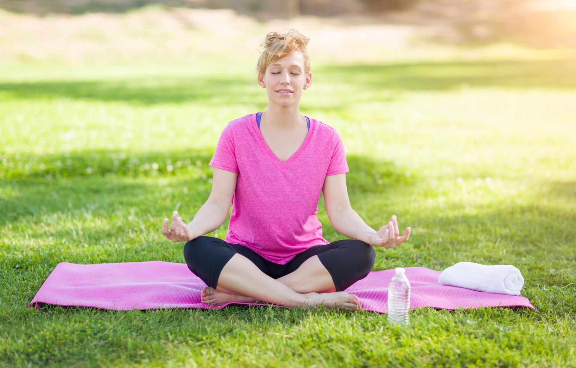 A woman is sitting on a yoga mat in a park