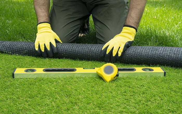 A man wearing yellow gloves is kneeling down next to a tape measure and a level