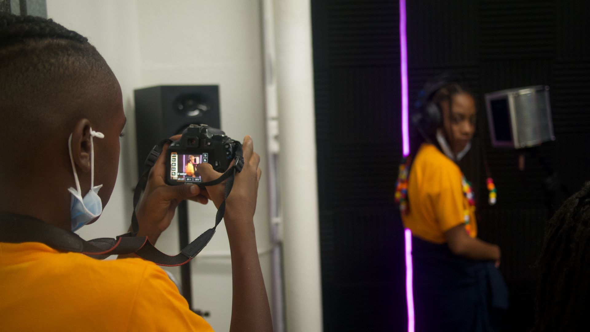 Person taking photo of another person recording music in a studio.