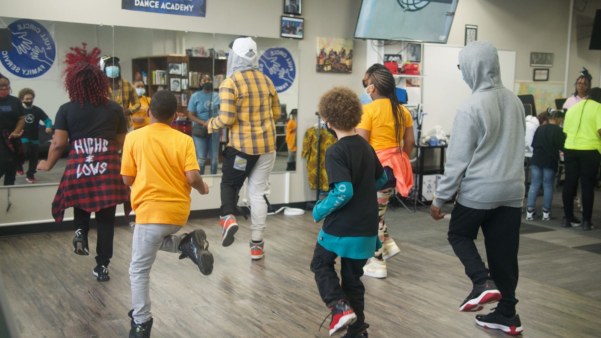 People dancing in a studio with a large mirror. Several wear bright colors, moving energetically.